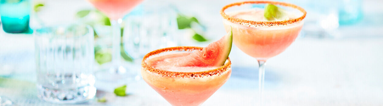 Salt-rimmed Margarita glasses filled with a pink, slushy version of a watermelon beergarita garnished with a small wedge of watermelon.